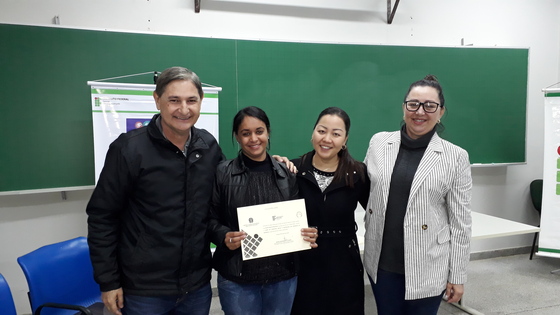 Estudante curso de Formação Inicial e Continuada em Contador de Histórias da turma de 2019 recebendo certificado de formatura junto com a diretora do campus (Bernardete Gaion), a coordenadora do curso (Jackeline Siraichi) e o professor Amir Limana.