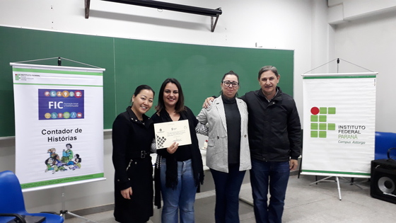 Estudante curso de Formação Inicial e Continuada em Contador de Histórias da turma de 2019 recebendo certificado de formatura junto com a diretora do campus (Bernardete Gaion), a coordenadora do curso (Jackeline Siraichi) e o professor Amir Limana.
