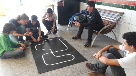 Estudantes no chão manuseando robô seguidor de linha branca em pista preta