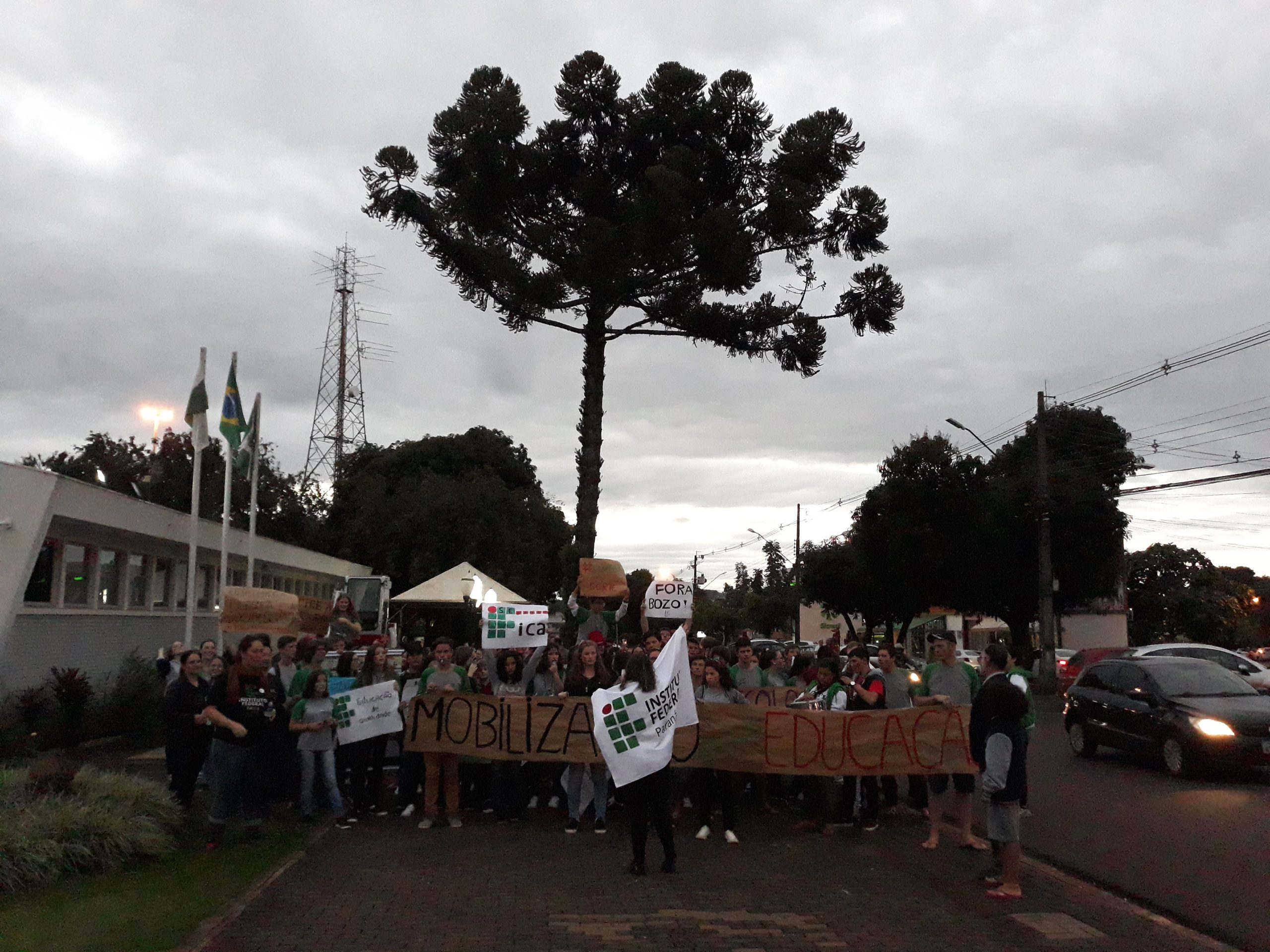 Os estudantes e servidores estão reunidos em frente à Prefeitura de Capanema, empunhando faixas de apoio à educação pública.