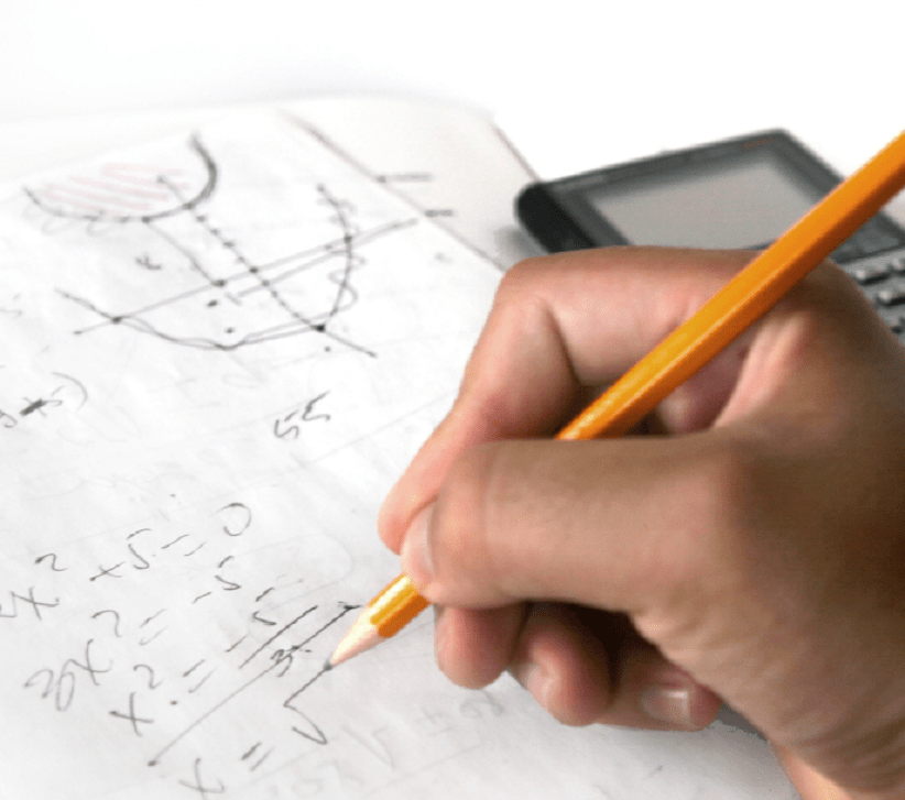 Fotografia de uma mão segurando um lápis do lado de uma calculadora fazendo conta sobre um papel quadriculado