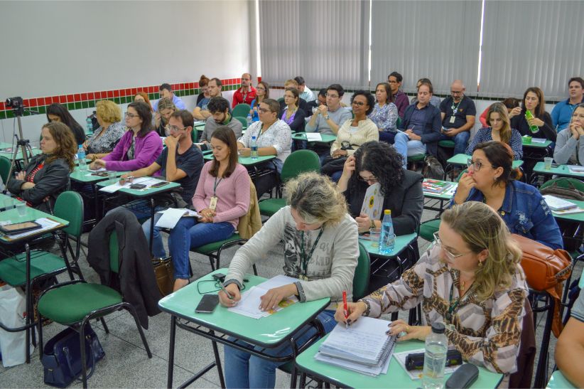 Foto de sala de aula com pessoas sentadas em carteiras olhando para frente