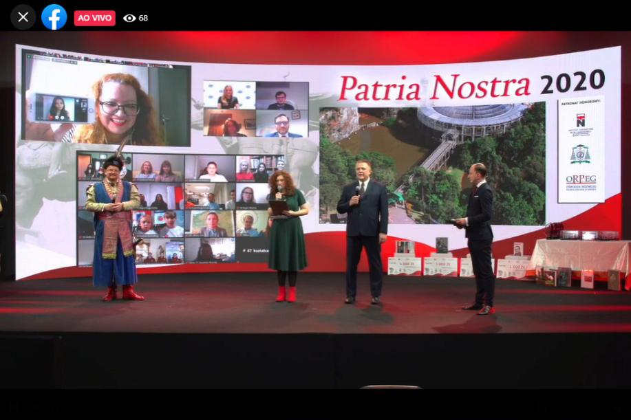 Na foto, há quatro personalidades polonesas em um palco de teatro; ao fundo, um grande telão com participantes do concurso em janelas de videoconferência