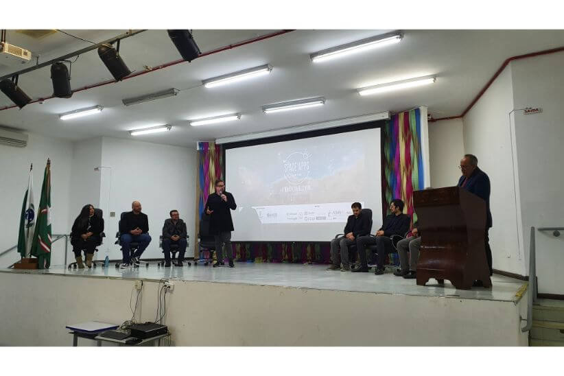Fotografia colorida em ambiente interno que mostra um grupo de oito pessoas no palco do auditório do Campus Curitiba.