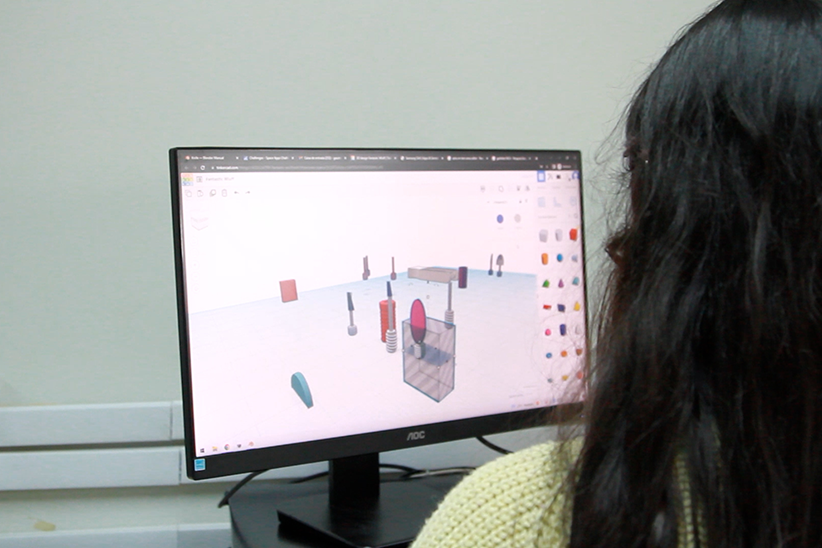 Foto de uma estudante de costas, olhando para a tela do computador com um programa do evento